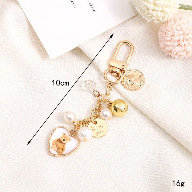 Cute bear keychain with a heart & bell charm, perfect unisex accessory for bags or gifts.