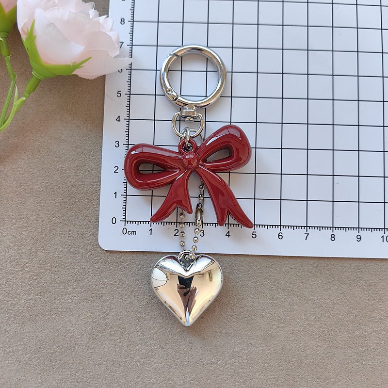 Pretty women's fashion keychain featuring a bow and heart charm. Lovely accessory for keys or bags.