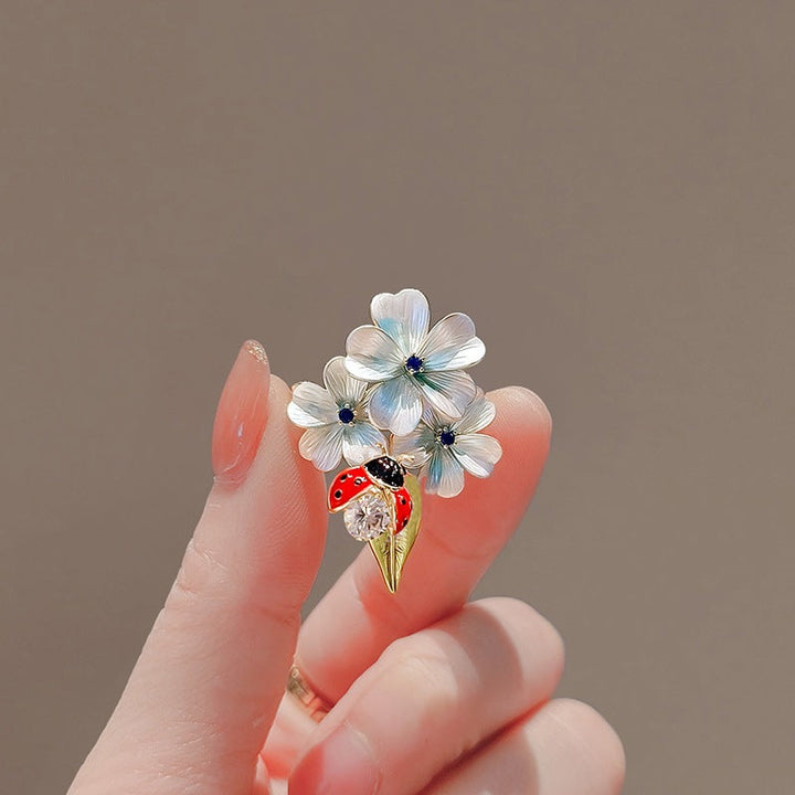 Stylish women's floral jewelry pin with a delicate ladybug, featuring lustrous crystals and enamel finish.