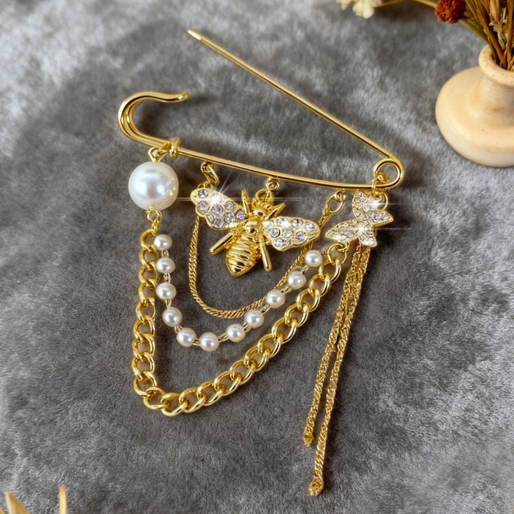 Stunning crystal & pearl bee brooch designed as a golden safety pin. A chic and elegant jewelry accessory.