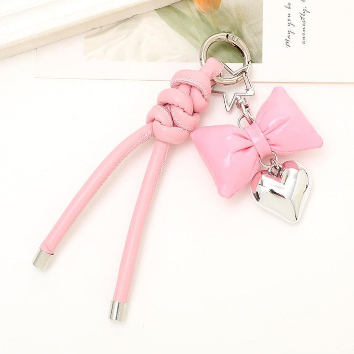 Hand holding an elegant bow & heart keychain, showing its size and detail.