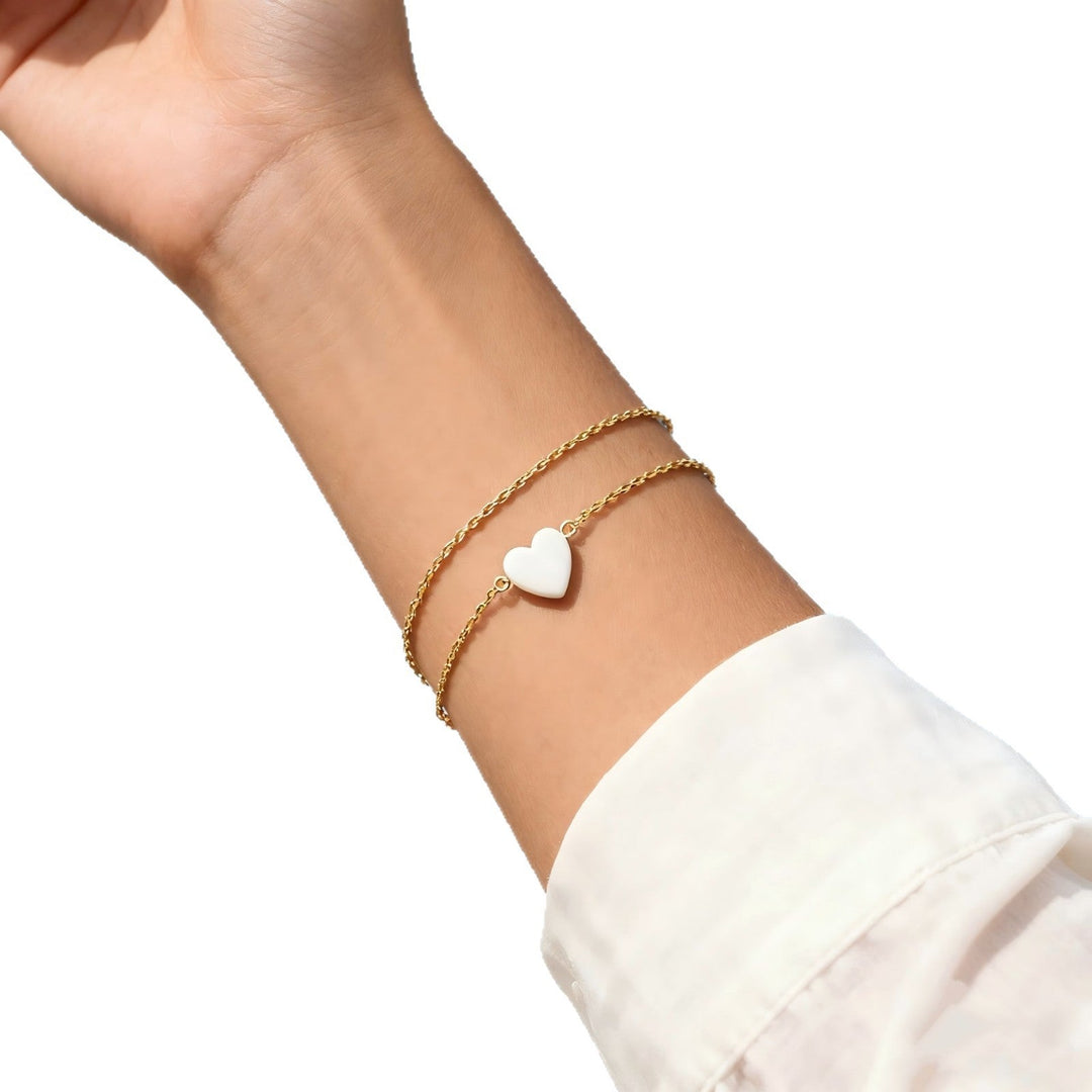 Women's elegant gold heart charm bracelet worn on wrist, showcasing its dainty and stackable design.