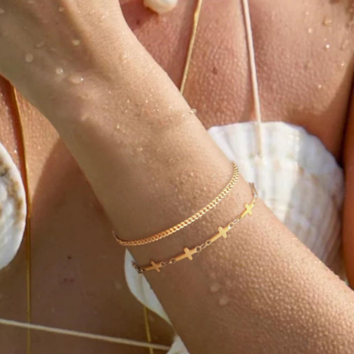 Women's multi-layered gold bracelet with a delicate cross charm and white pearls. Adjustable elegant jewelry.