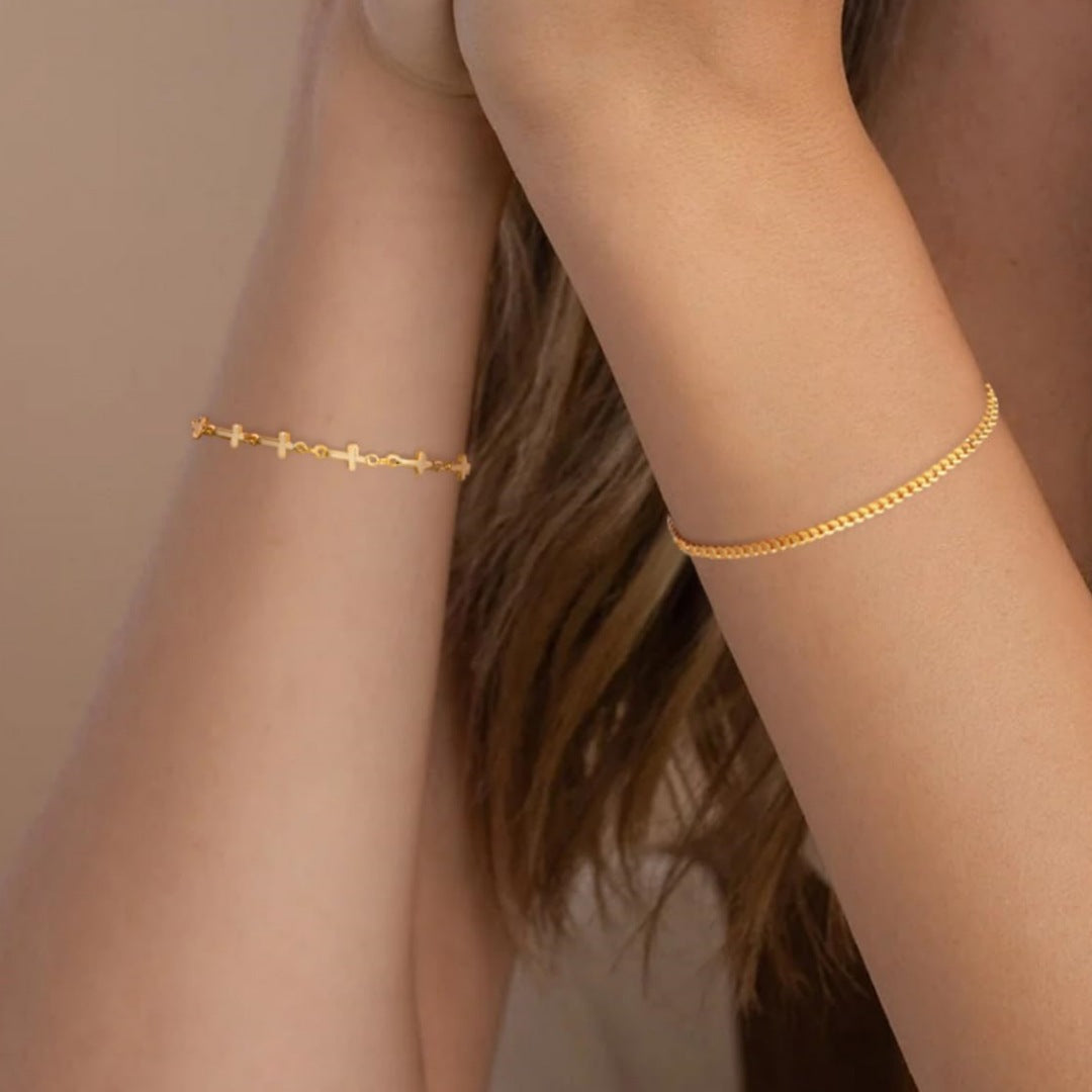 Spiritual women's gold layered bracelet, featuring a prominent cross charm and small white beads. Adjustable fit.