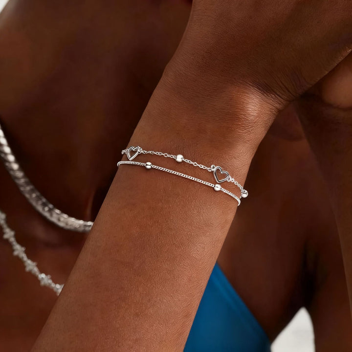 Chic gold tone layered bracelet for women, adorned with a delicate heart charm. Perfect elegant jewelry accessory.