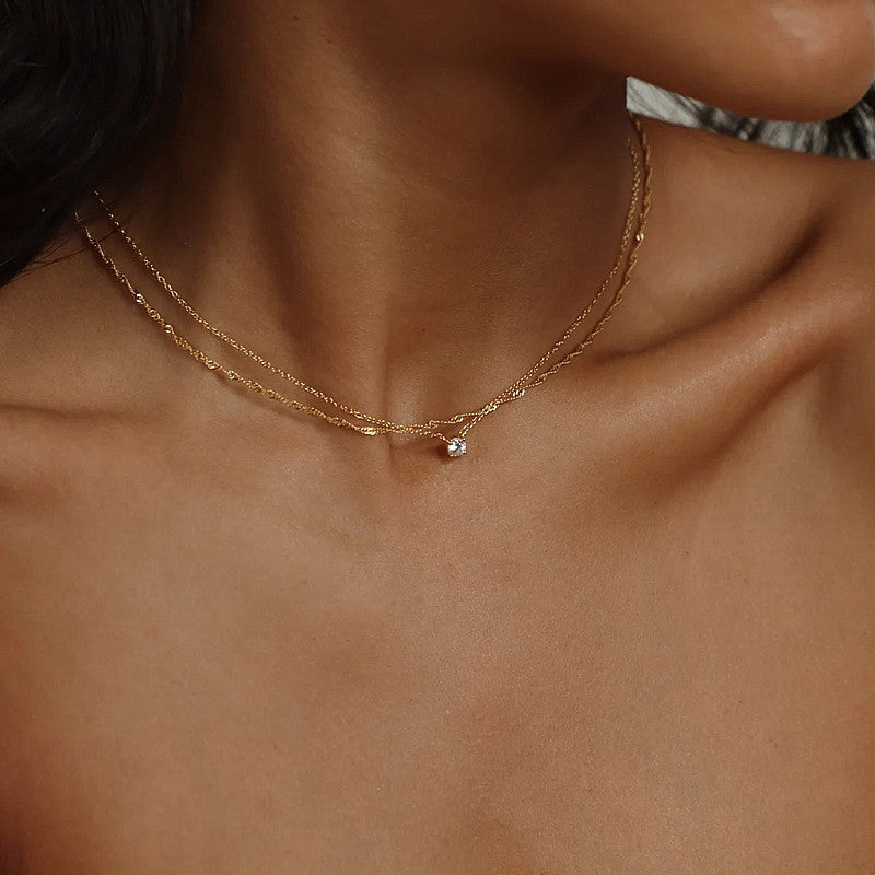 Close-up of a women's gold layered necklace with white plating, a chic and delicate jewelry piece.