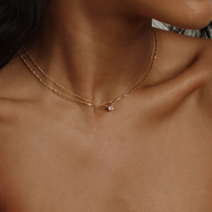 Close-up of a women's gold layered necklace with white plating, a chic and delicate jewelry piece.