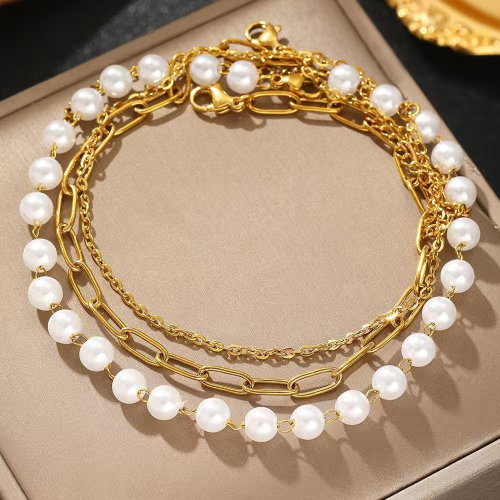 Women's elegant layered bracelet set featuring delicate pearls & gold-tone chains. Stylish fashion accessory.