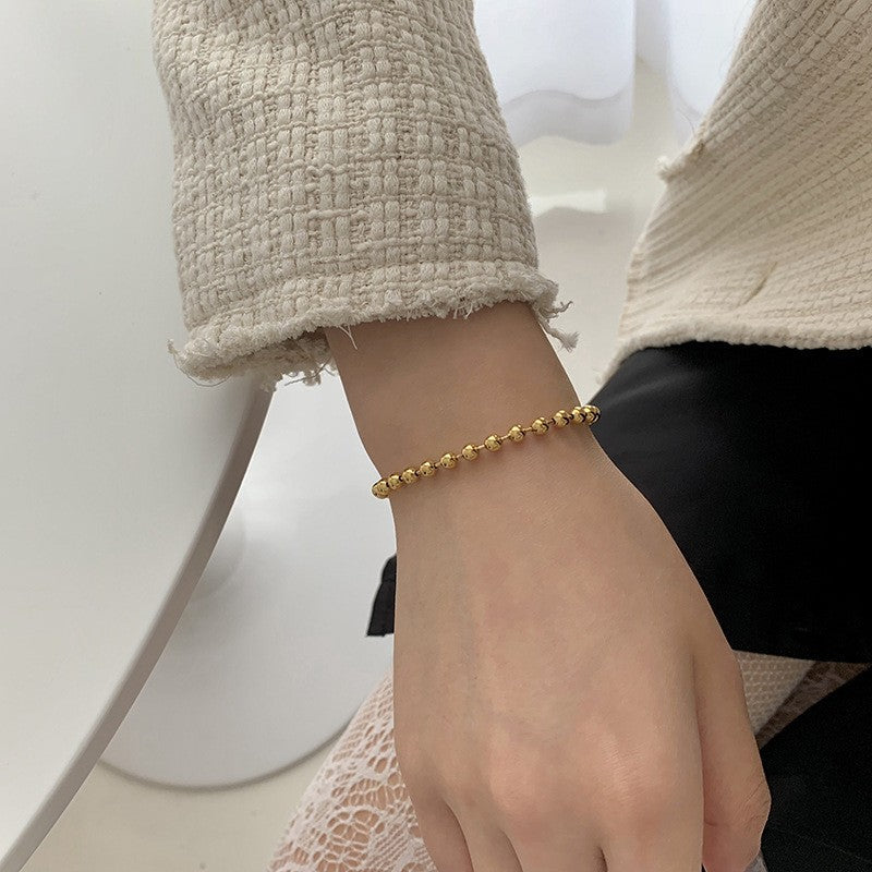 Close-up of a women's elegant beaded bracelet featuring gold & white charms, a chic jewelry accessory.