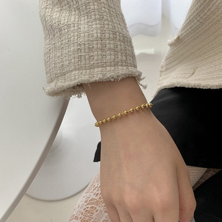 Close-up of a women's elegant beaded bracelet featuring gold & white charms, a chic jewelry accessory.