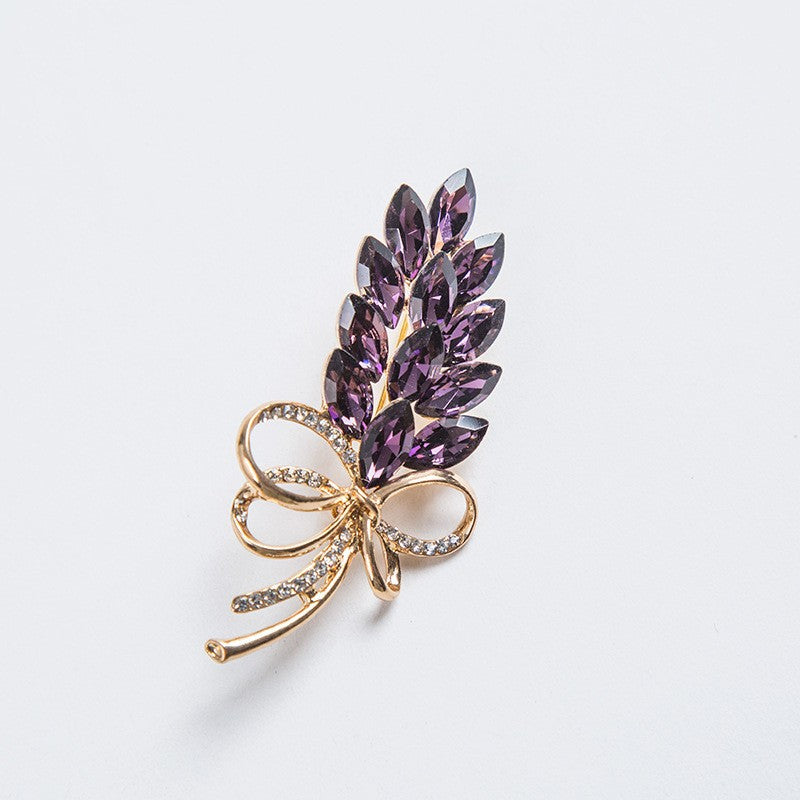 Shimmering crystal leaf brooch with bow accent for women. Elegant fashion accessory, perfect for any outfit.