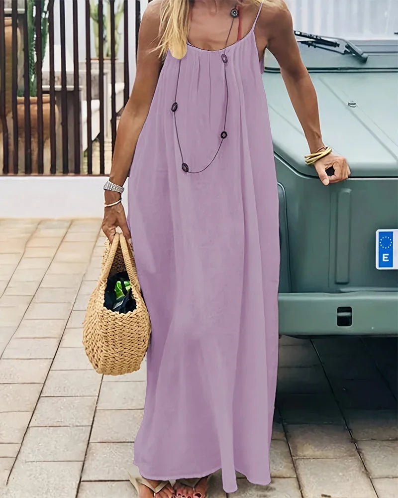 Woman wearing an elegant flowing cami maxi dress, sleeveless, walking on the beach, vacation style.