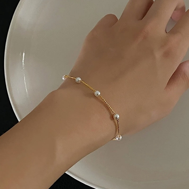 Women's elegant gold chain bracelet with lustrous pearls worn on a wrist. Dainty & adjustable fashion jewelry.