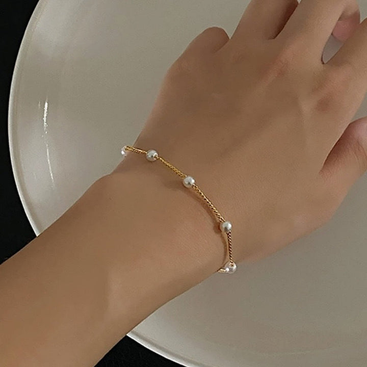 Women's elegant gold chain bracelet with lustrous pearls worn on a wrist. Dainty & adjustable fashion jewelry.