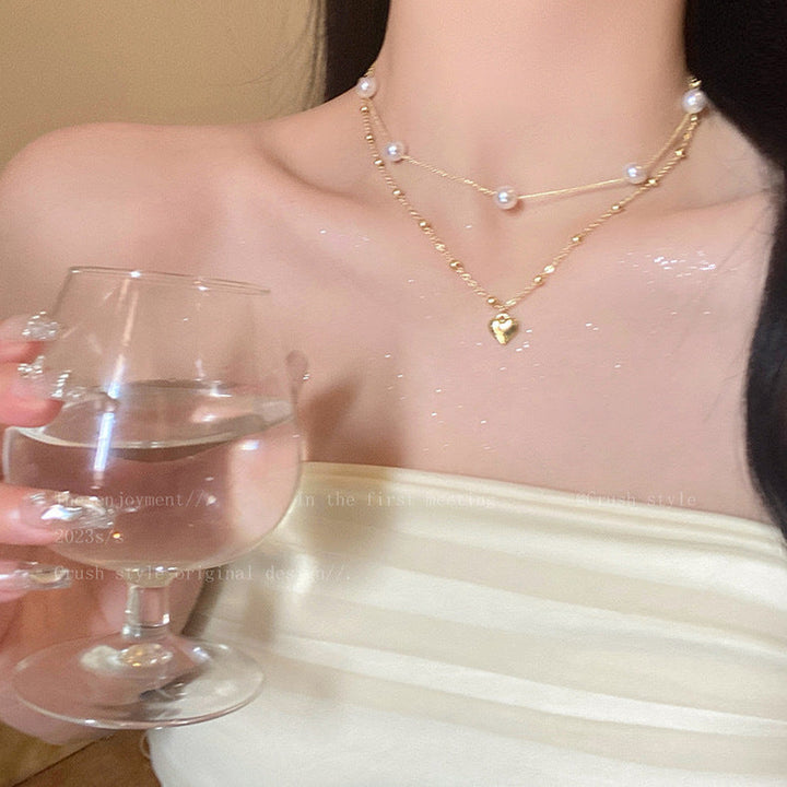 Elegant women's layered necklace with a heart charm and pearl color accents. Perfect fashion jewelry accessory.