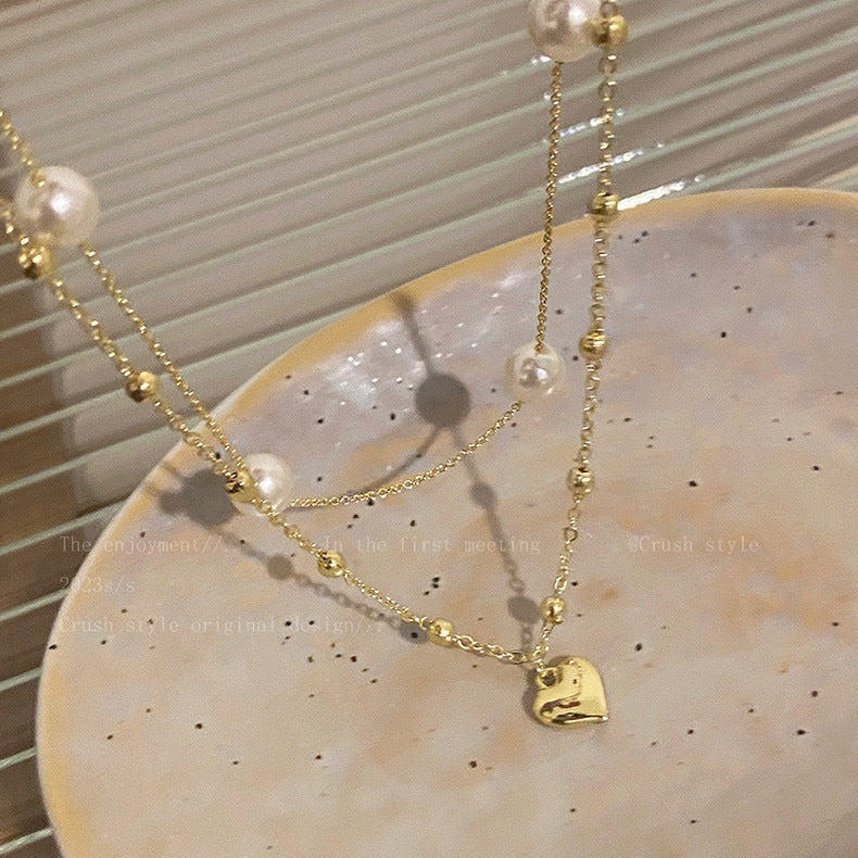 Chic women's layered necklace featuring a delicate heart charm and lustrous pearl-color beads. Adjustable fashion jewelry.