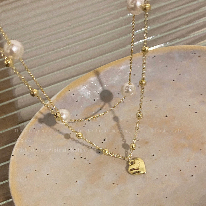 Chic women's layered necklace featuring a delicate heart charm and lustrous pearl-color beads. Adjustable fashion jewelry.