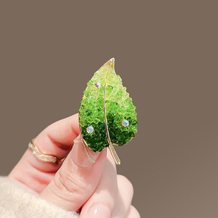 Close-up of gold-tone nature-inspired leaf brooch with intricate design and sparkling crystal details.