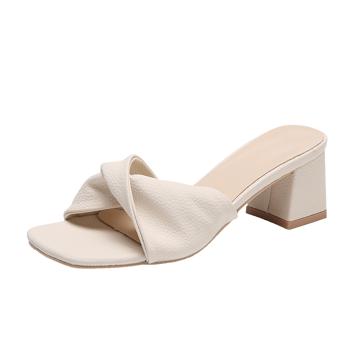 Open-toe women's block heel mule sandals featuring a chic twisted strap. Dressy slip-on heels for elegant comfort.