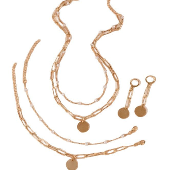 Fashionable women's pearl & gold chain jewelry set, including a chic layered necklace, bracelet, and earrings.