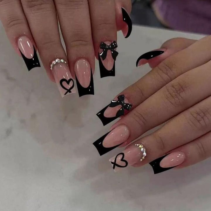 Stylish press-on nails for women, featuring a unique black tip design, bows, and heart nail art.