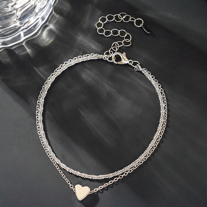 Dainty two-tone heart charm anklet on a woman's ankle, a stylish silver & gold adjustable summer accessory.