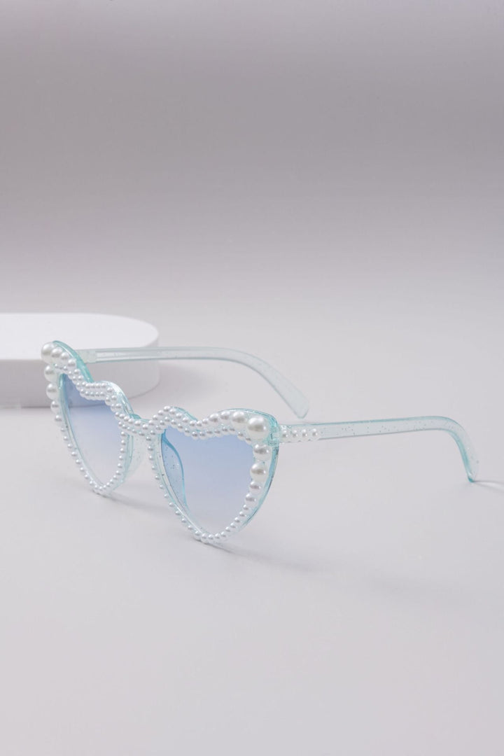 Close-up: glamorous heart-shaped women's sunglasses showcasing delicate pearl accents, fashion eyewear.