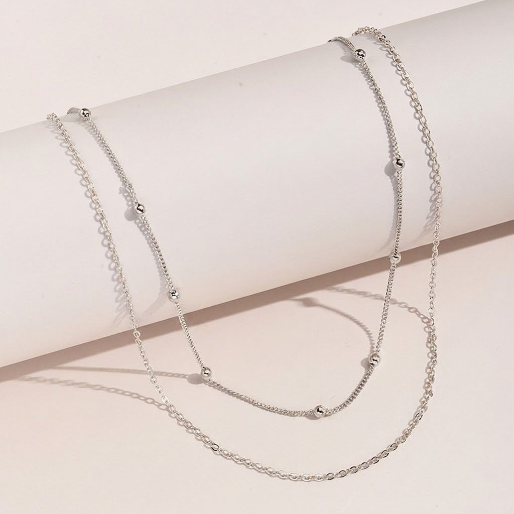 Fashionable women's gold layered necklace featuring white elements, an elegant accessory.