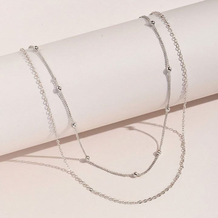 Fashionable women's gold layered necklace featuring white elements, an elegant accessory.