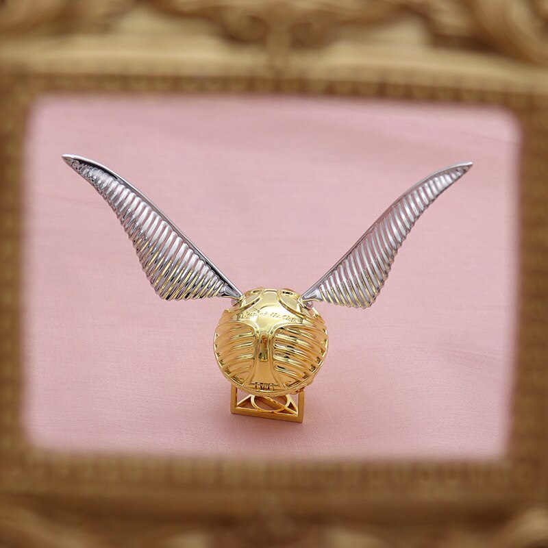 Close-up of a golden winged orb ring box, intricate details & movable design.