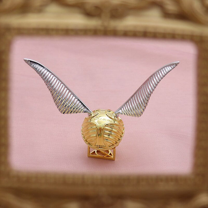 Close-up of a golden winged orb ring box, intricate details & movable design.