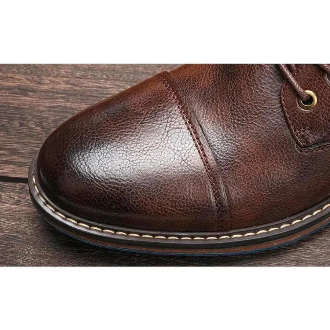 Close-up of men's sleek black leather lace-up ankle boots, showing cap toe detail and quality craftsmanship.
