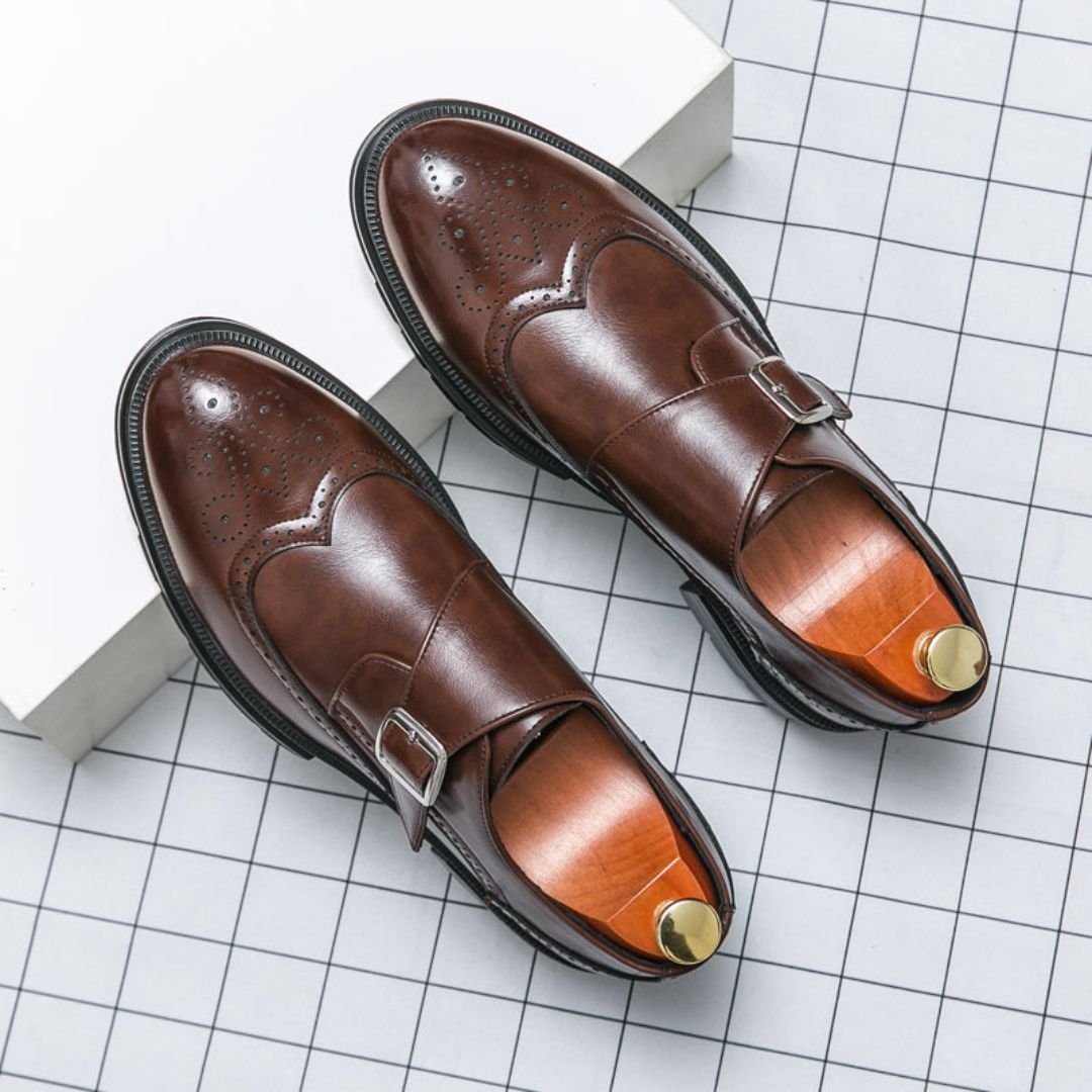 Detailed view of a men's tan leather monk strap brogue dress shoe, showcasing wingtip and perforation patterns.