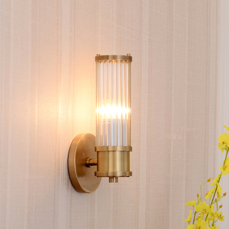 Stylish modern wall fixture: gold base, crystal cylinder shade, brightens your indoor space.