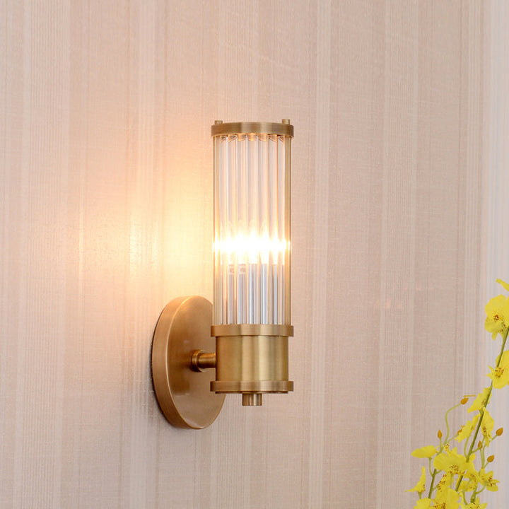 Stylish modern wall fixture: gold base, crystal cylinder shade, brightens your indoor space.