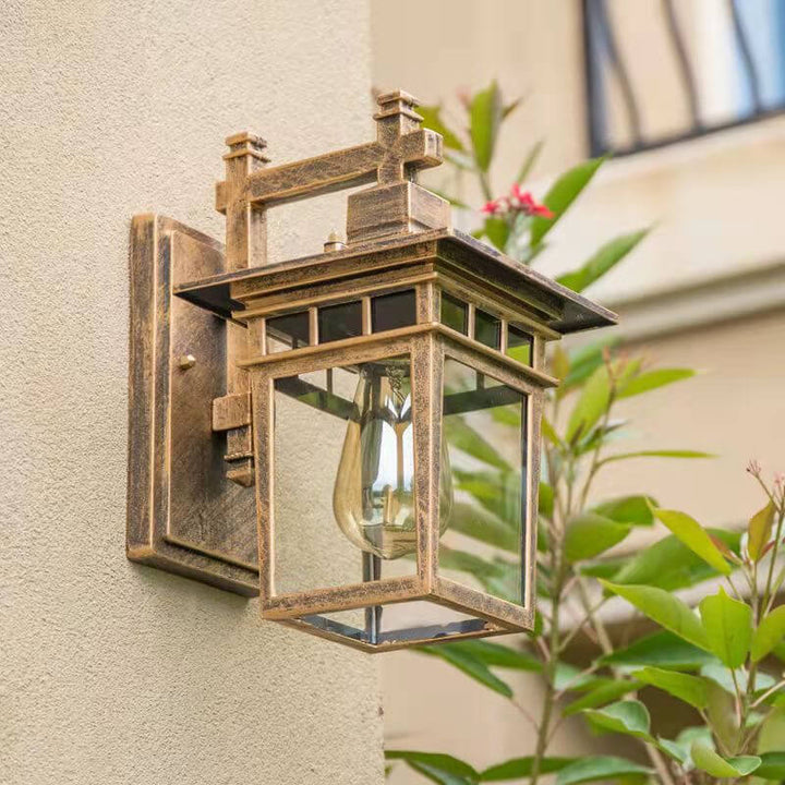 Black aluminum outdoor lantern wall light installed on a brick garden wall, providing ambient lighting.