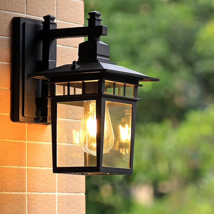 Outdoor black lantern wall light next to garden plants, providing ambient waterproof lighting.