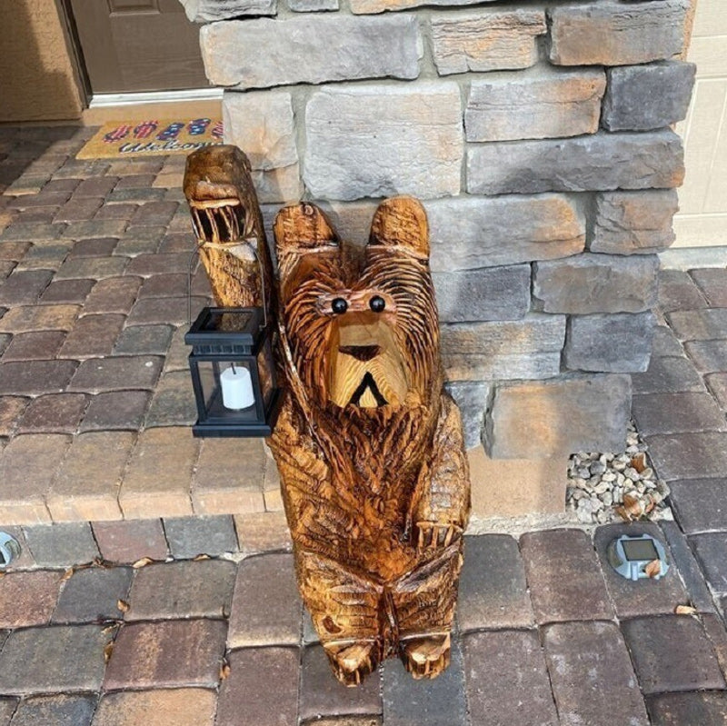 Bear solar garden lantern nestled among plants, casting a warm flickering LED glow, ideal outdoor lighting.