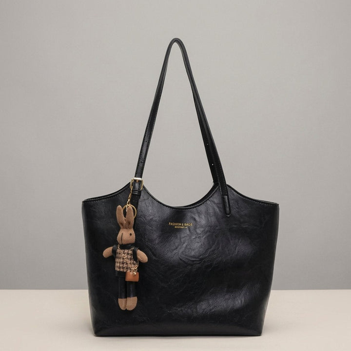 Woman models a stylish soft vegan leather shoulder tote bag, accented with a charming bunny detail.
