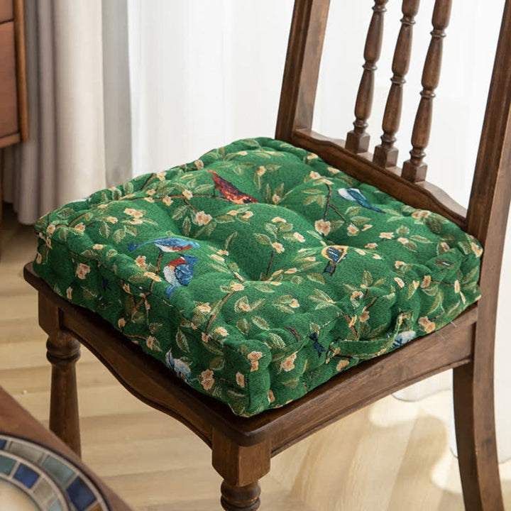 Thick outdoor patio chair cushion with ties & a decorative bird leaf print, providing comfy extra padding.