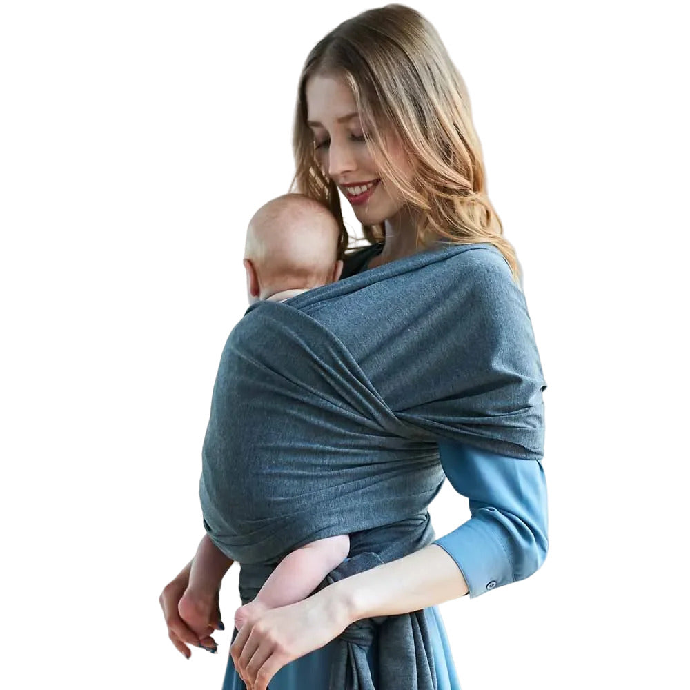 Happy baby snugly nestled in a grey cotton wrap carrier, providing ergonomic support and comfort for both infant and adult.