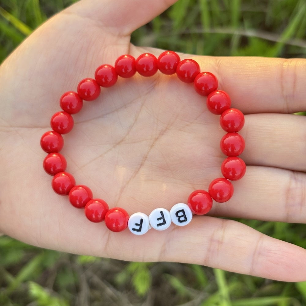 Close-up of a pastel bead friendship bracelet, showing 'LOVE' lettering and elastic band. Dainty beaded jewelry.