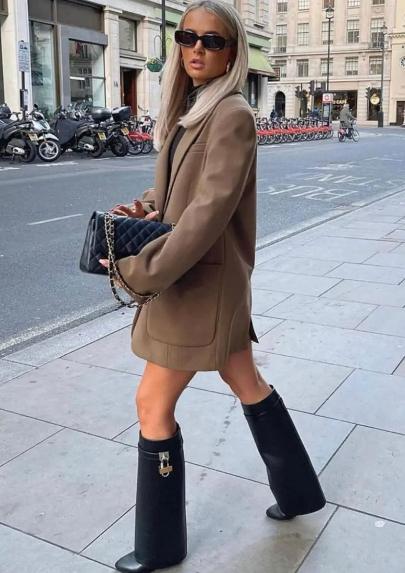 Full-length view of women's black glossy sculptural wedge knee-high boots, luxurious and modern.