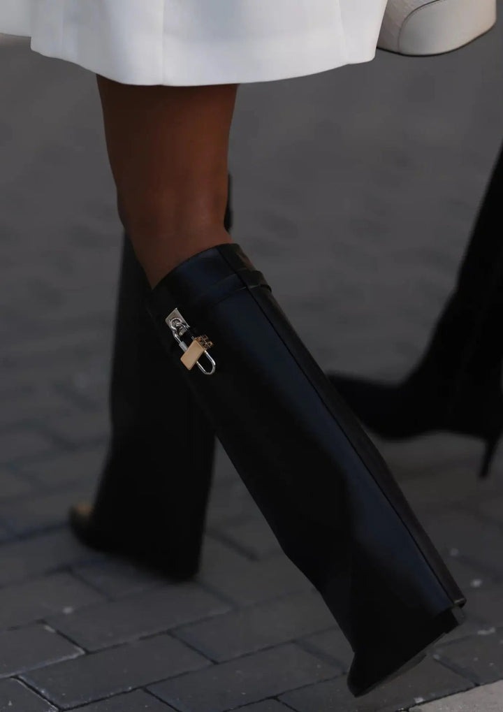 Close-up of the unique sculptural wedge heel on women's black glossy knee-high boots.