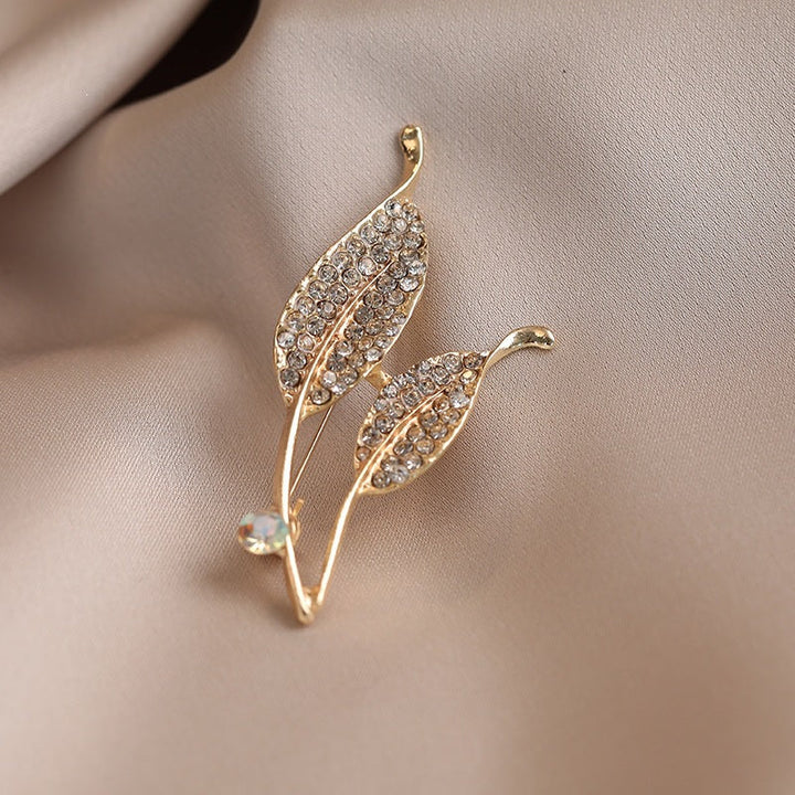 Sparkling crystal leaf brooch, a chic gold-finish women's fashion accessory. Ideal as a statement lapel pin.