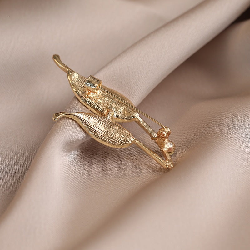 Gold-tone elegant leaf lapel pin adorned with shimmering crystals, enhancing any women's outfit.