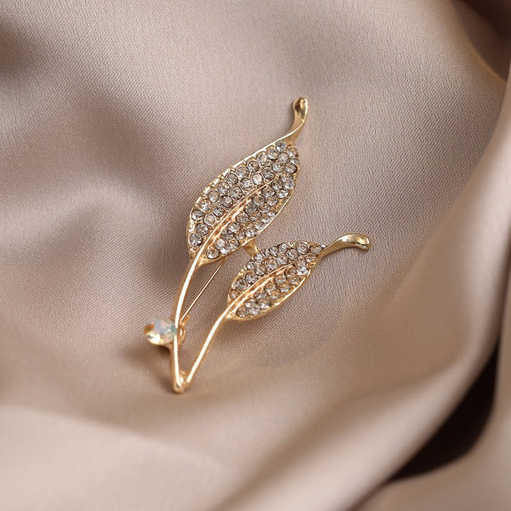 Intricate crystal leaf design brooch with a radiant gold finish, a sophisticated women's jewelry piece.
