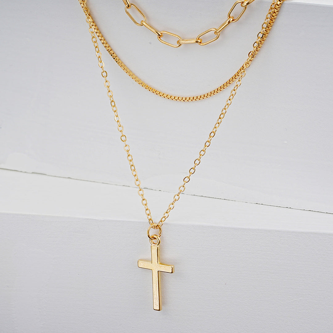 Close-up of a women's gold-tone multi-layered necklace with a detailed cross pendant. Chic fashion jewelry.