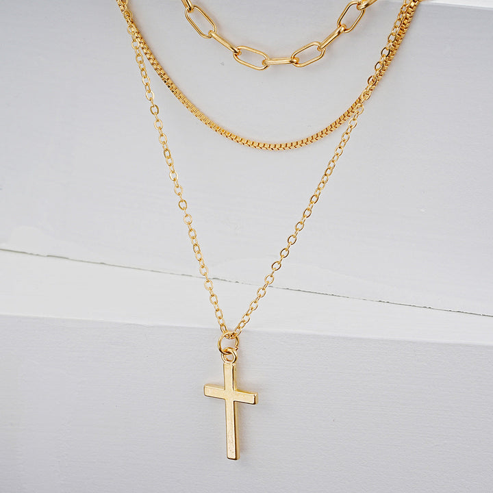 Close-up of a women's gold-tone multi-layered necklace with a detailed cross pendant. Chic fashion jewelry.