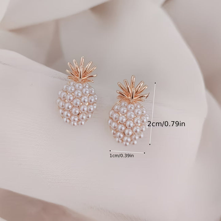 Close-up of women's tropical-style pearl and pineapple drop earrings, elegant jewelry.